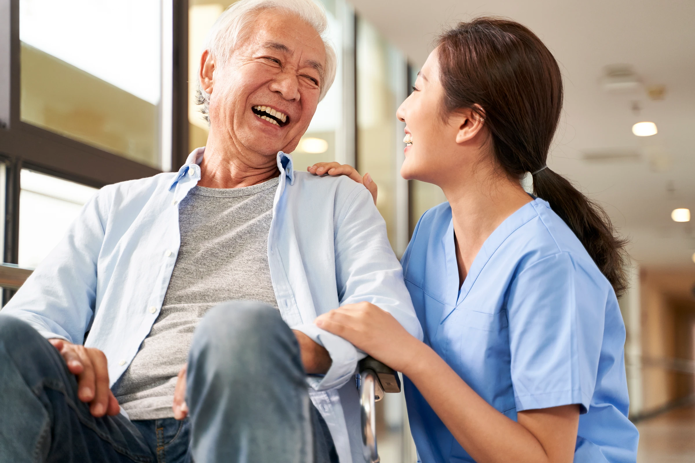 Une infirmière souriante partageant un moment chaleureux avec une patiente âgée qui rit