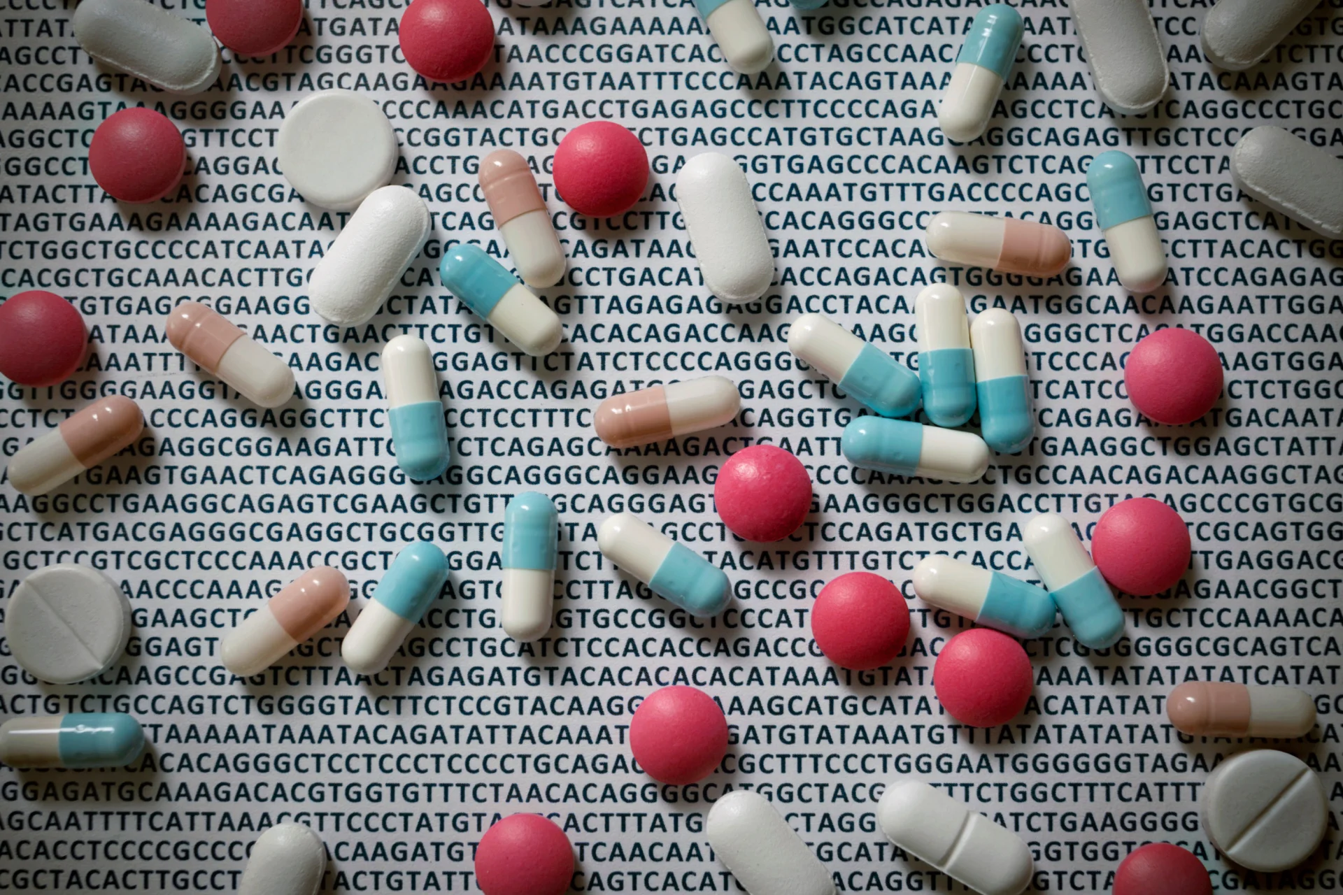 Des comprimés éparpillés sur un fond de lettres de paires de bases d’ADN répétées, illustrant le lien entre le code génétique et la réponse aux médicaments.